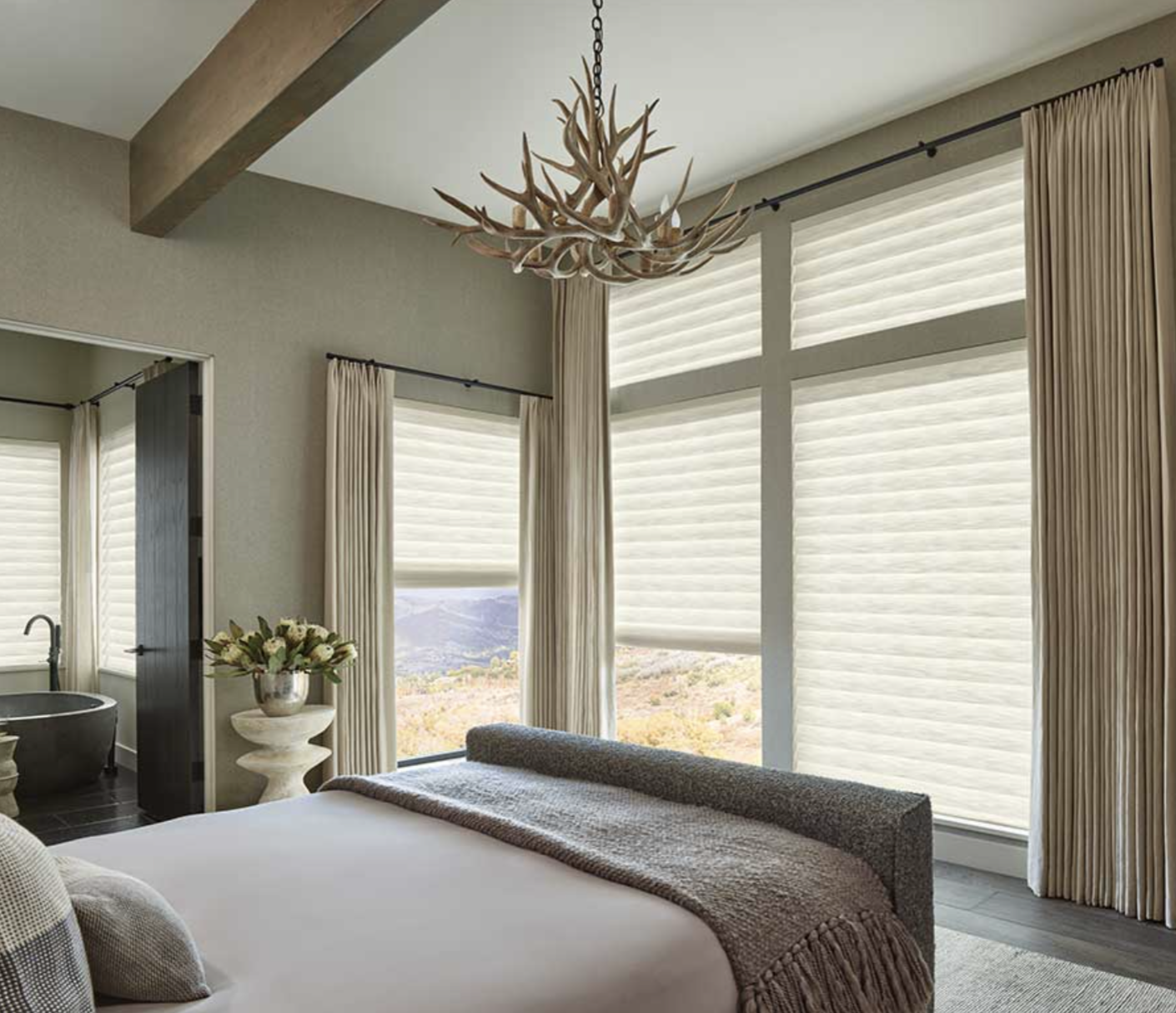 Calming bedroom that has a neutral palette It has Aura Illuminated Shades at differing heights on the right and back windows.