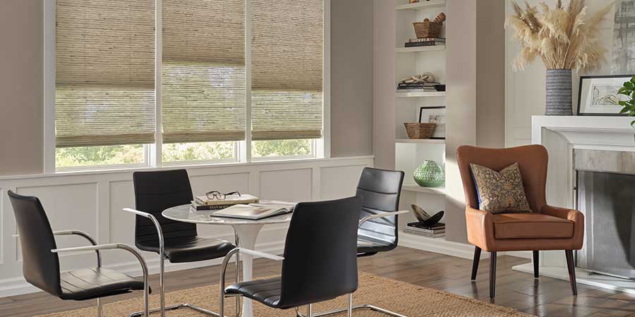 Provenance® Woven Woods in a sitting room. They are covering three windows and each are lowered at varying lengths with the far left and far right at the same length.