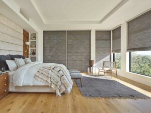 A neutral bedroom with alustra woven texture shades cascaded on two walls of windows in a neurtal bedroom