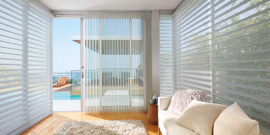 A modern living area with a low-profile couch that covers the entire length of one wall. The Silhouette Window Shades are covering windows that lead out to a backyard with a pool