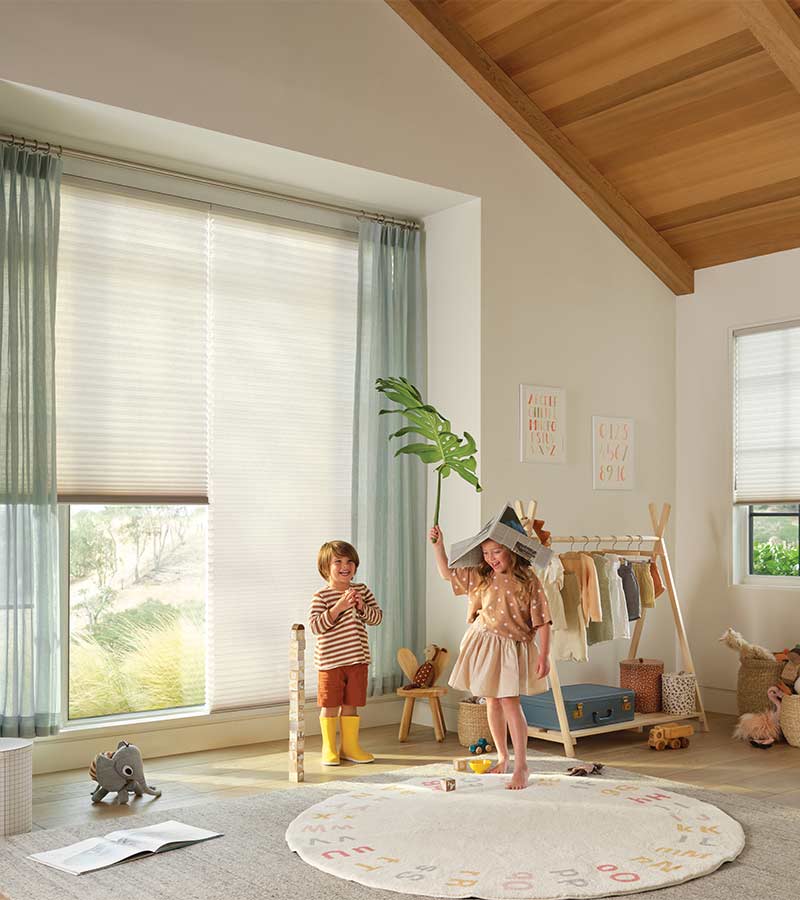 little kids playing in front of large window covered by cellular shade and drapery in modern playroom