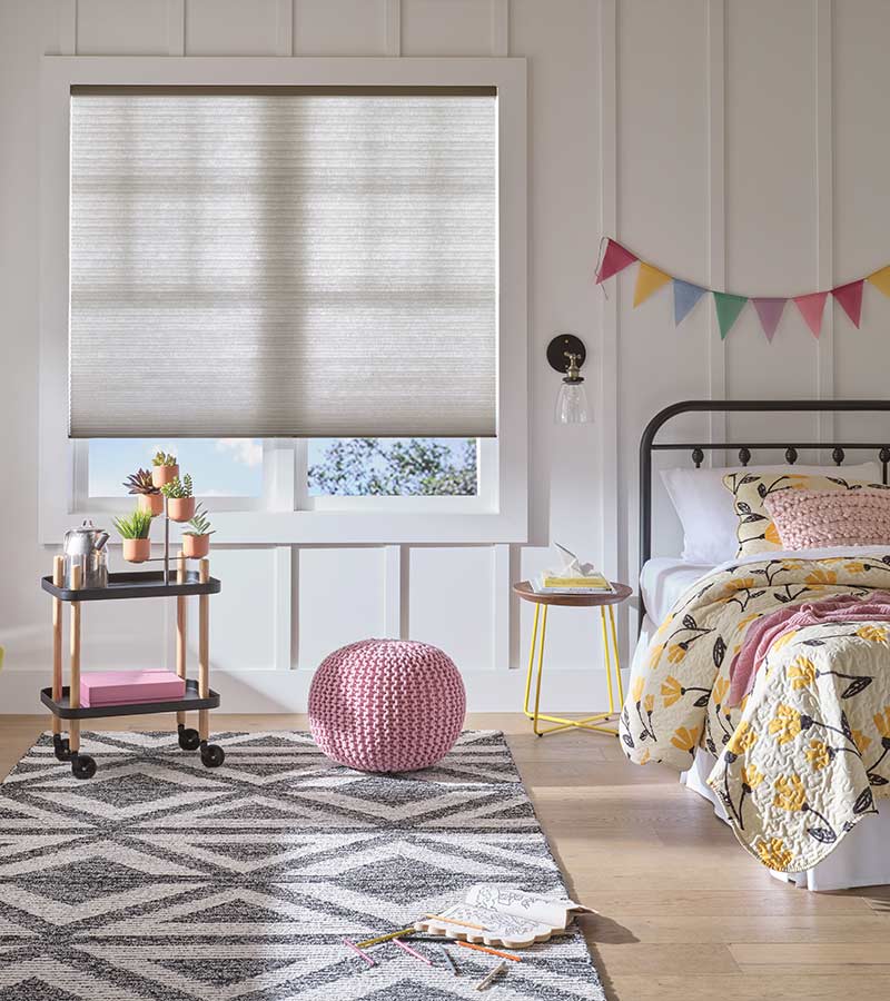 coloring book on floor of little girl bedroom gray window shade halfway closed and large pink pouf chair